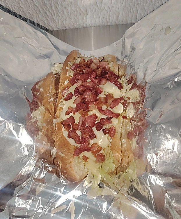 Hot dog con tocineta, queso y salsa blanca envuelto en papel aluminio